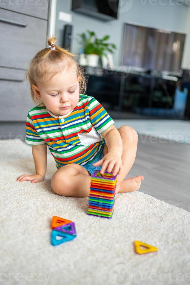 pequeño niña jugando vistoso imán el plastico bloques equipo a hogar. el niño jugando educativo juegos. temprano infancia desarrollo. foto