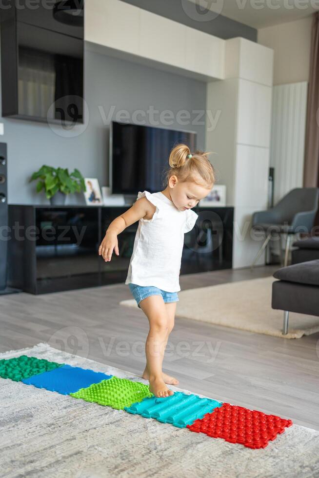 Little girl walks on a massage mat. Toddler baby foot massage mat. Exercises for legs orthopedic massage carpet. photo