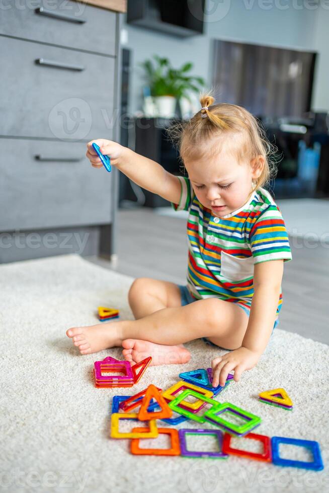 pequeño niña jugando vistoso imán el plastico bloques equipo a hogar. el niño jugando educativo juegos. temprano infancia desarrollo. foto