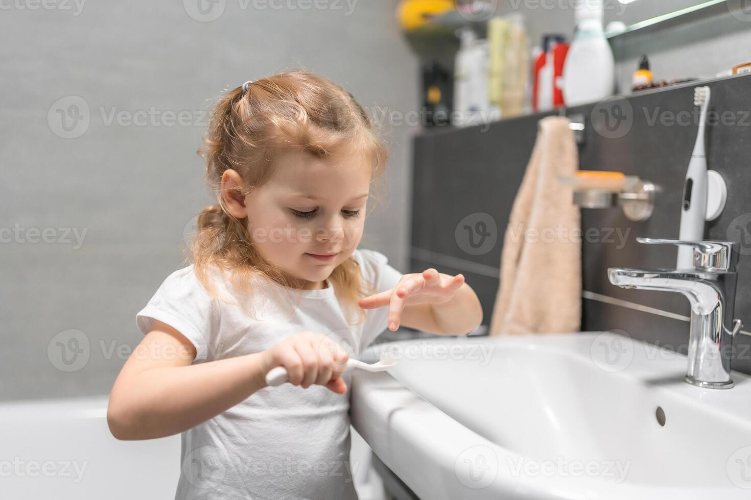 Happy toddler girl brushing teeth in the bath photo