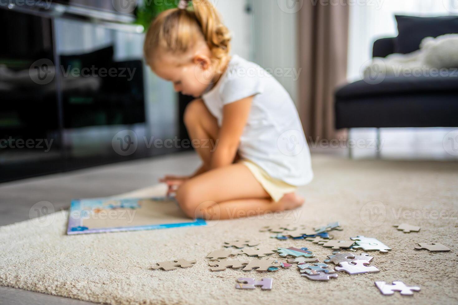 Little blonde girl sits at home on the carpet and collects puzzles photo