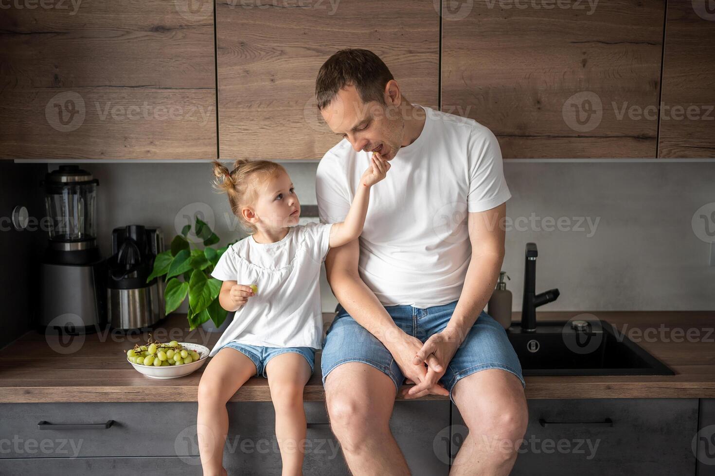 Cute little girl and her handsome dad are eating fruit in modern kitchen. Healthy eating. photo