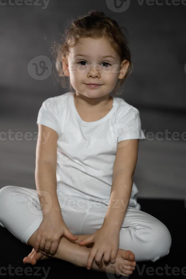 Little cute girl practicing yoga pose on grey background in dark room photo