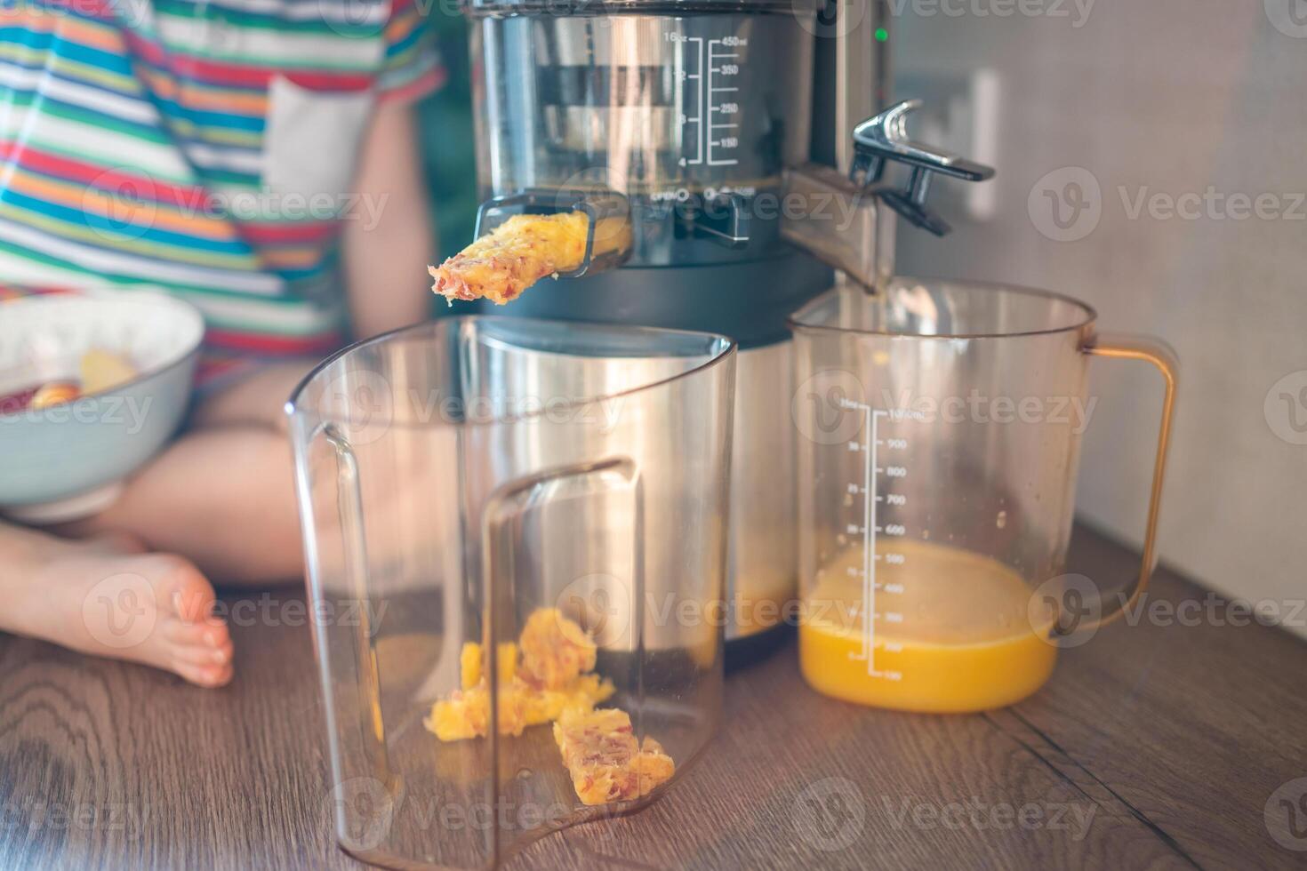 Little girl making fresh juice on the table in home kitchen. Focus on juicer photo