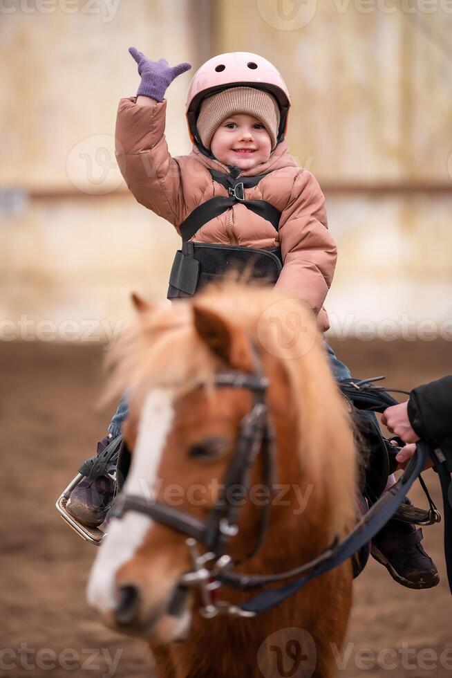 Little Child Riding Lesson. Three-year-old girl rides a pony and does exercises. High quality photo