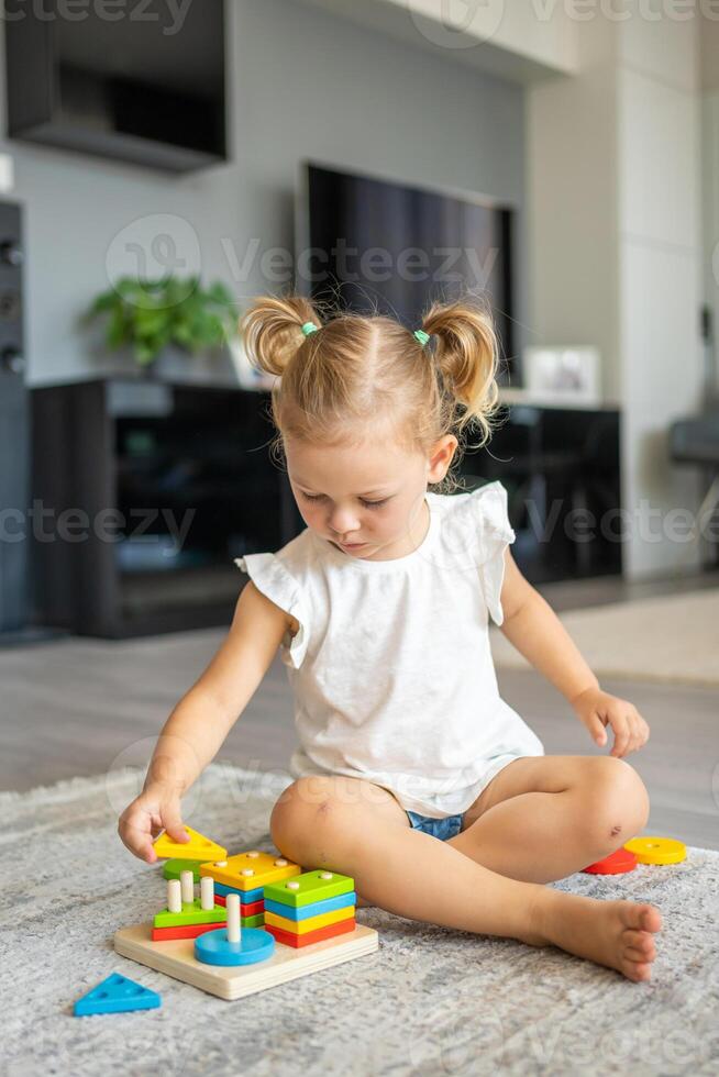 linda caucásico pequeño niña jugando en el piso a hogar con eco de madera juguetes montessori juguete. el niño jugando educativo juegos. foto