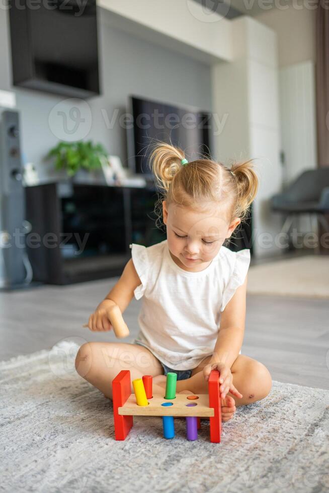 Cute caucasian little girl playing on the floor at home with eco wooden toys. The child playing educational games. photo