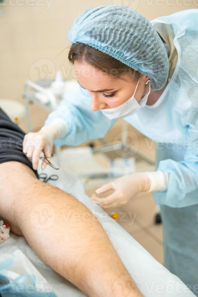 Dermatologist surgeon stitching up a wound after skin surgery, close up view of operation process photo
