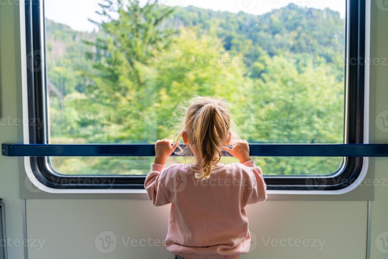 Beautiful little girl looking out train window outside, while it moving. Traveling by railway in Europe photo