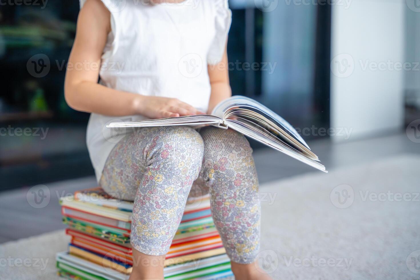 Close up view of Little girl is sitting on stack of children's books and leafing through a book with fairy tales photo