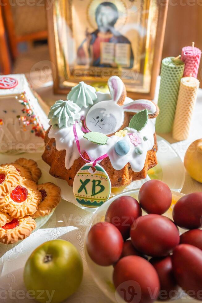 Easter cake with painted eggs, apples and cookies on table in home kitchen. Church icons and candle on background. Orthodox religion theme. photo