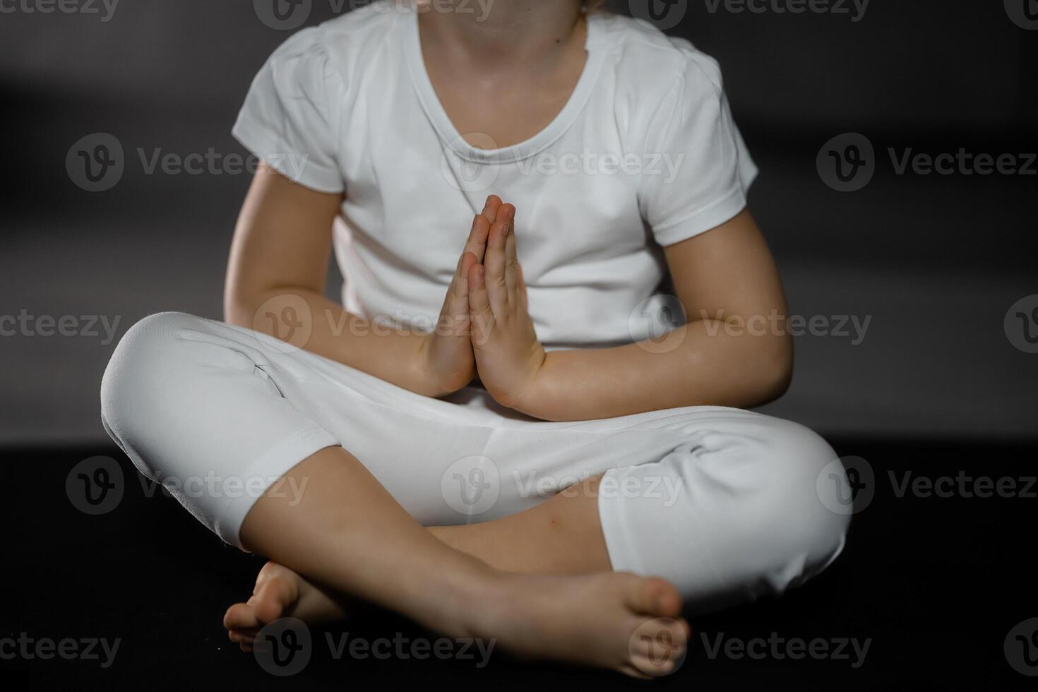 Three years old little girl meditating in a lotus pose on a gray background in dark room photo