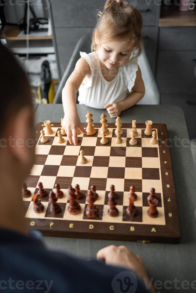 Little girl playing chess with her father at the table in home kitchen. The concept early childhood development and education. Family leisure, communication and recreation. photo