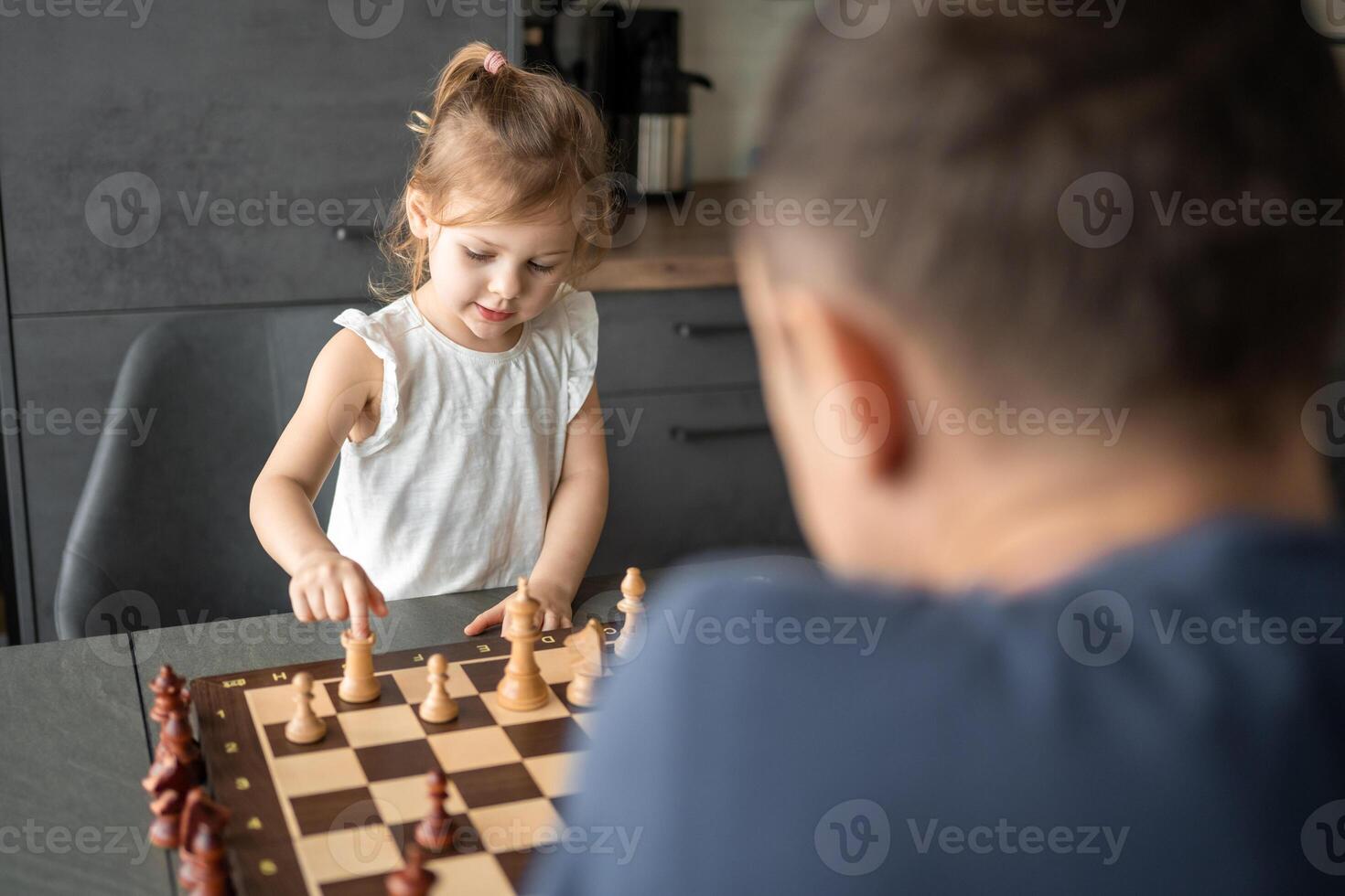 padre enseñando su pequeño hija a jugar ajedrez a el mesa en hogar cocina. el concepto temprano infancia desarrollo y educación. familia ocio, comunicación y recreación. foto