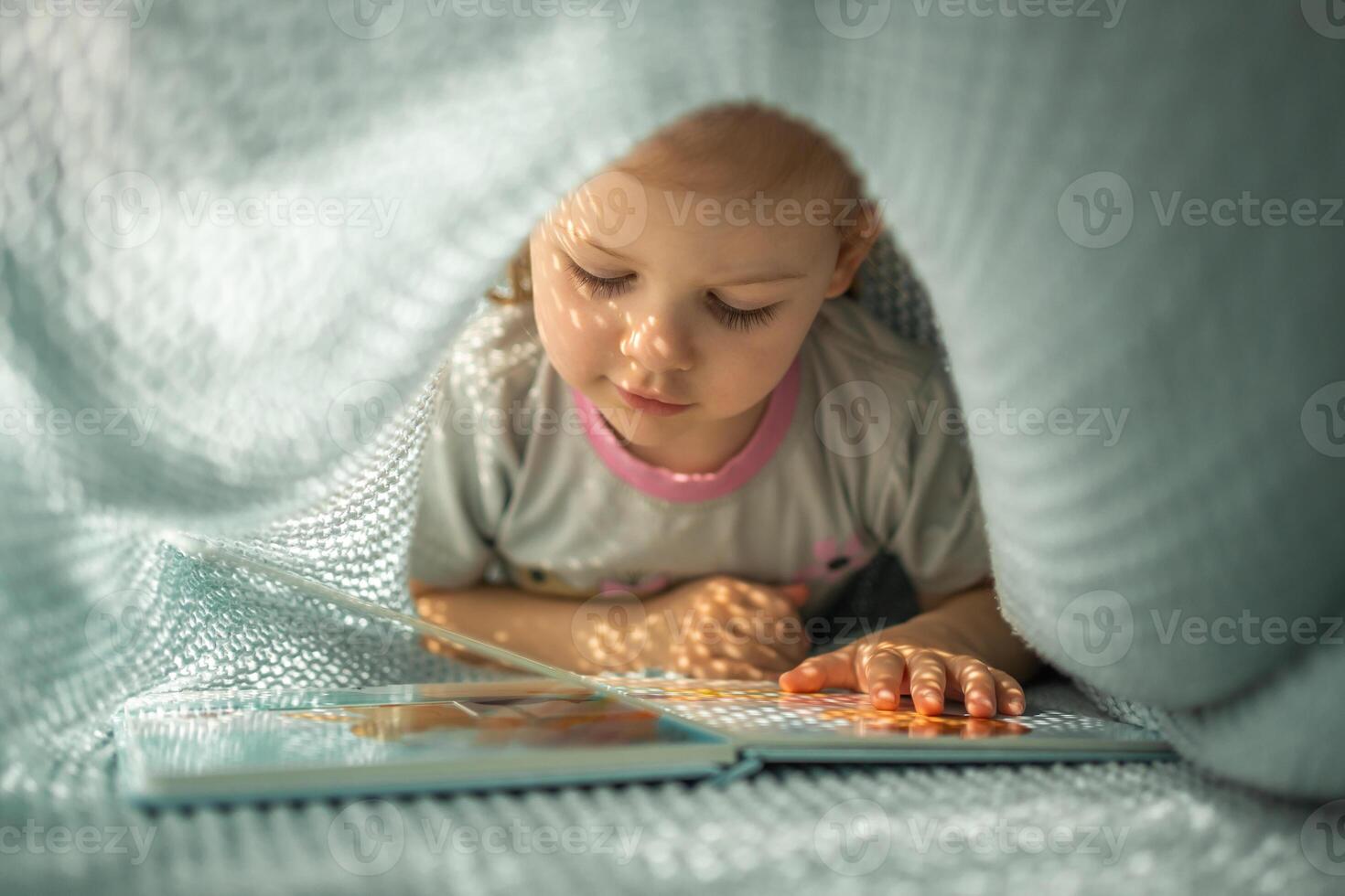 pequeño niña disfrutando de revisión un libro debajo azul de punto tartán en soleado Mañana foto