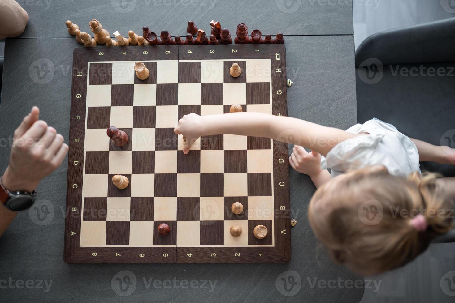 padre enseñando su pequeño hija a jugar ajedrez a el mesa en hogar cocina. el concepto temprano infancia desarrollo y educación. familia ocio, comunicación y recreación. foto