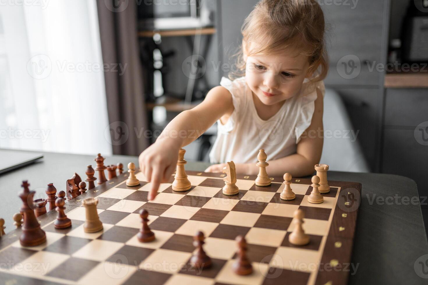 Little girl playing chess at the table in home kitchen. The concept early childhood development and education. Family leisure, communication and recreation. photo