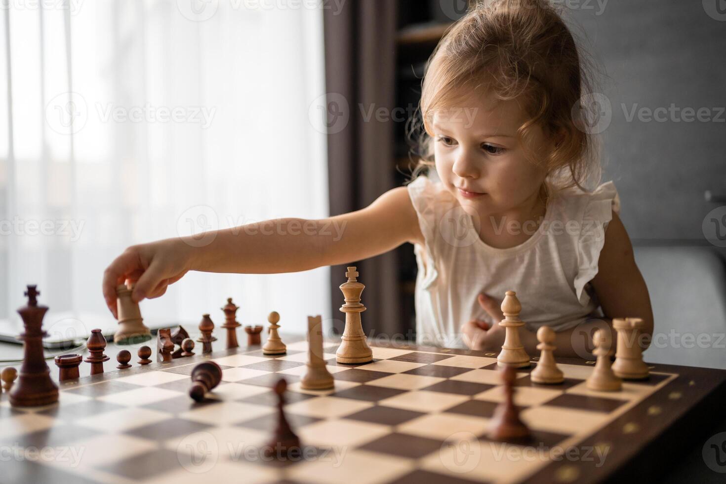 pequeño niña jugando ajedrez a el mesa en hogar cocina. el concepto temprano infancia desarrollo y educación. familia ocio, comunicación y recreación. foto