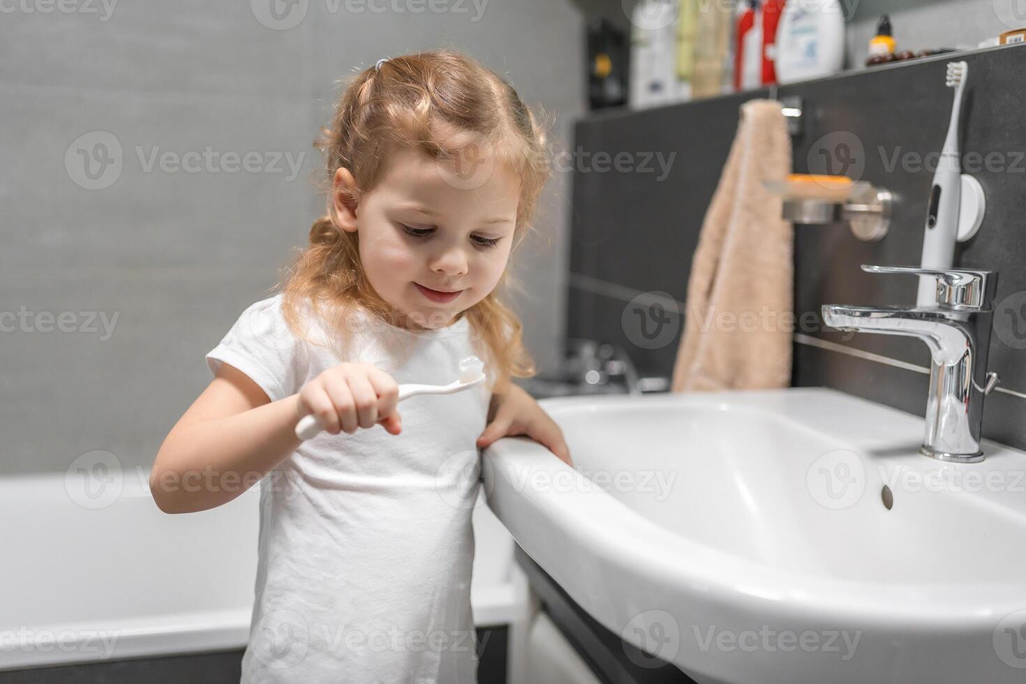 Happy toddler girl brushing teeth in the bath photo