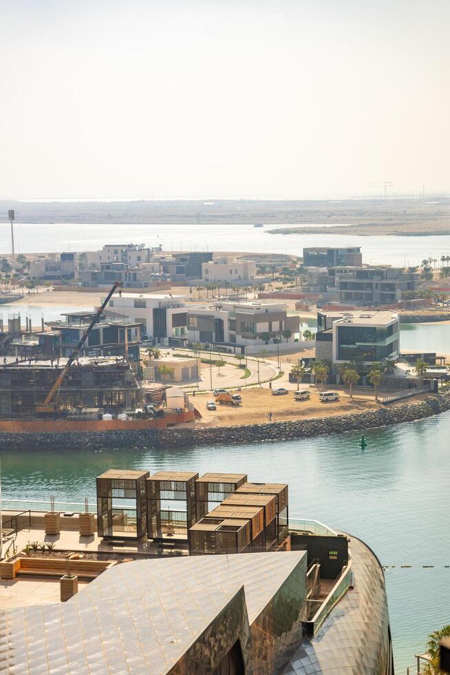 Abu Dhabi, United Arab Emirates - December 4, 2023. New buildings surrounded with construction cranes at the island seen at the background of sea in Abu Dhabi photo
