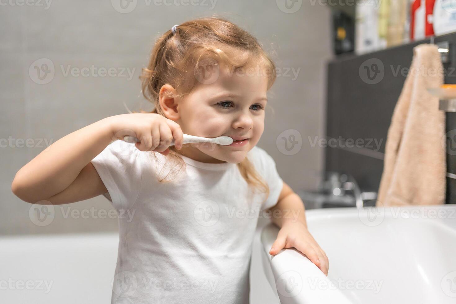 Happy toddler girl brushing teeth in the bath photo