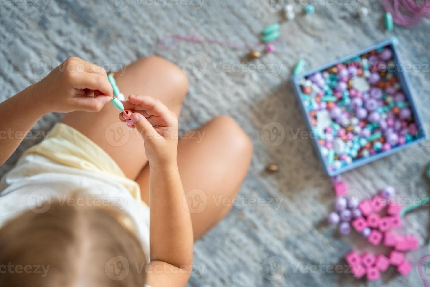 Little girl making wooden beads bracelet at home living room. Children's creativity and the development of fine motor skills photo