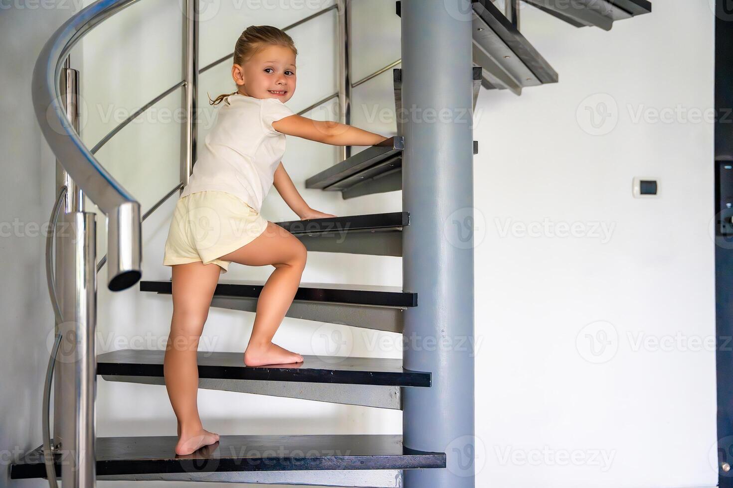 Little girl going up the stairs at modern home, child climbing spiral staircase. Dangerous situation at home. Child safety concept. photo