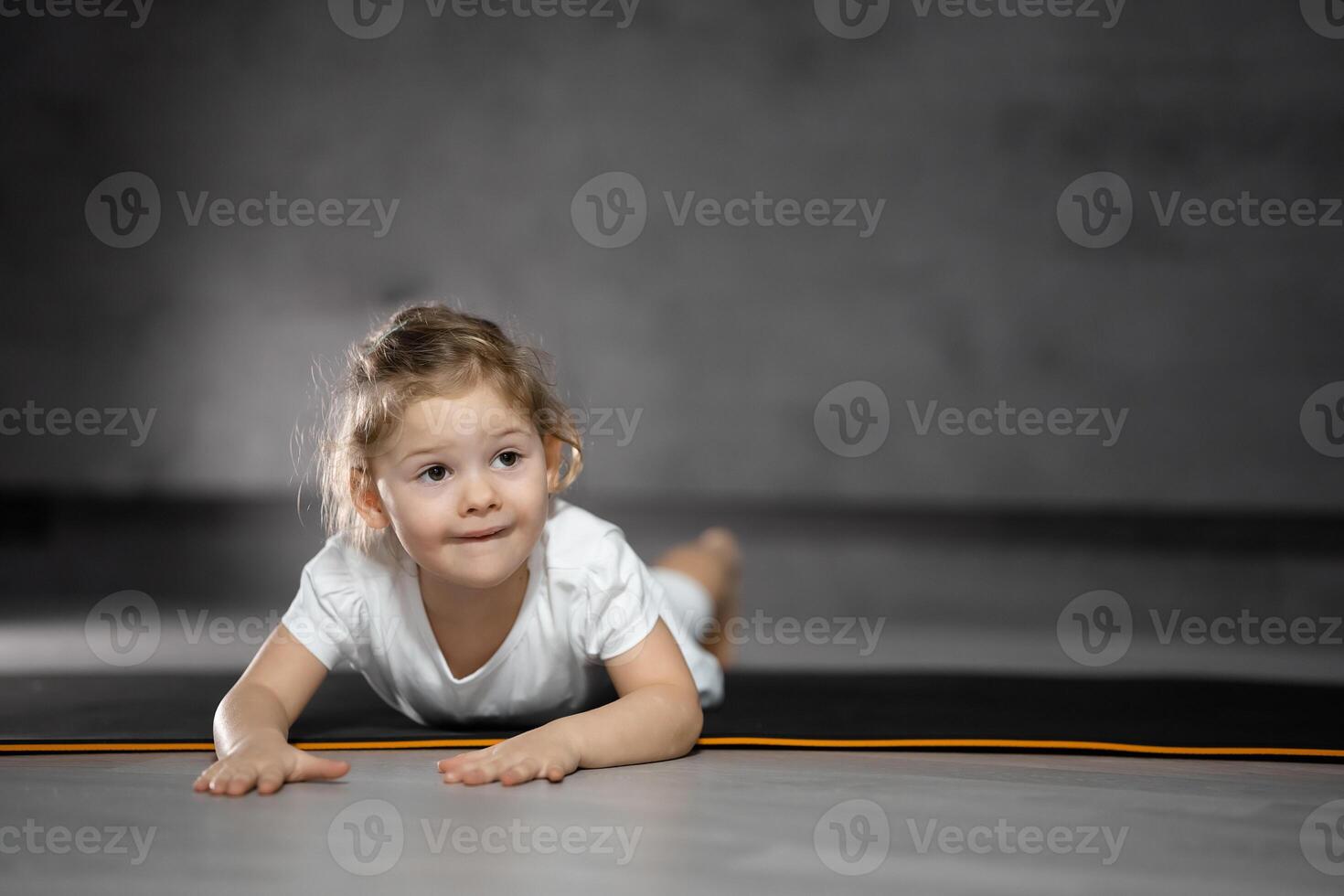 Little cute girl practicing yoga pose on grey background in dark room. High quality photo