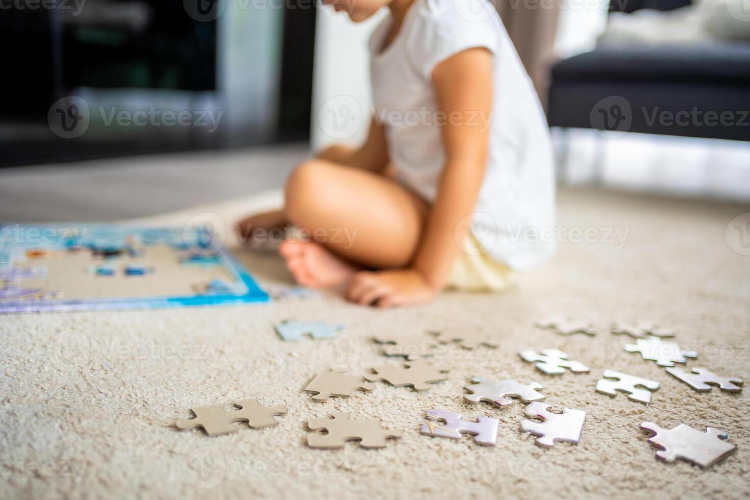 Little blonde girl sits at home on the carpet and collects puzzles. Focus on the puzzle pieces photo