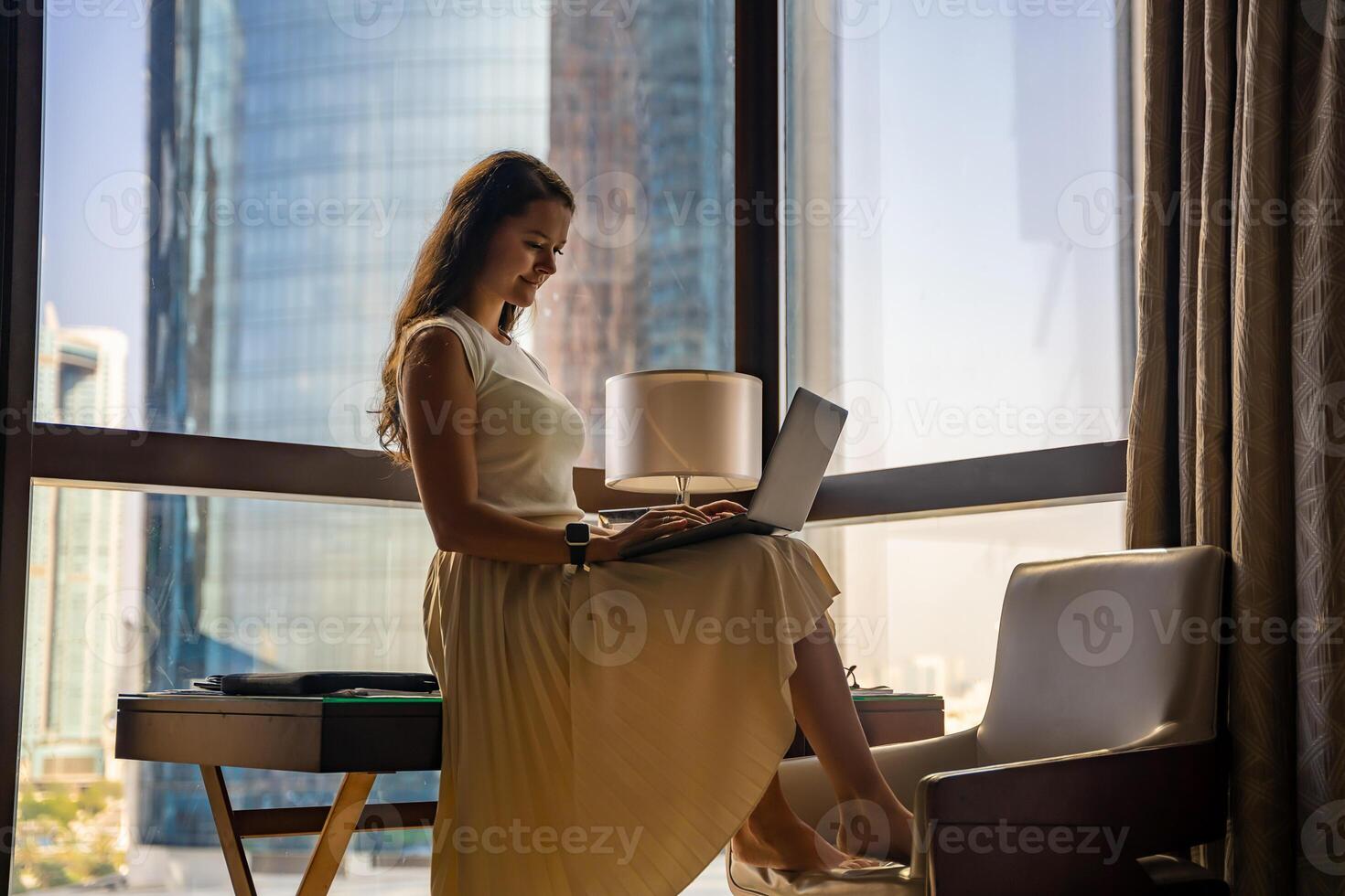 Stylish businesswoman freelancer working with laptop and she is sitting on the table, enjoying panoramic view in the city background. Low key photo. High quality photo