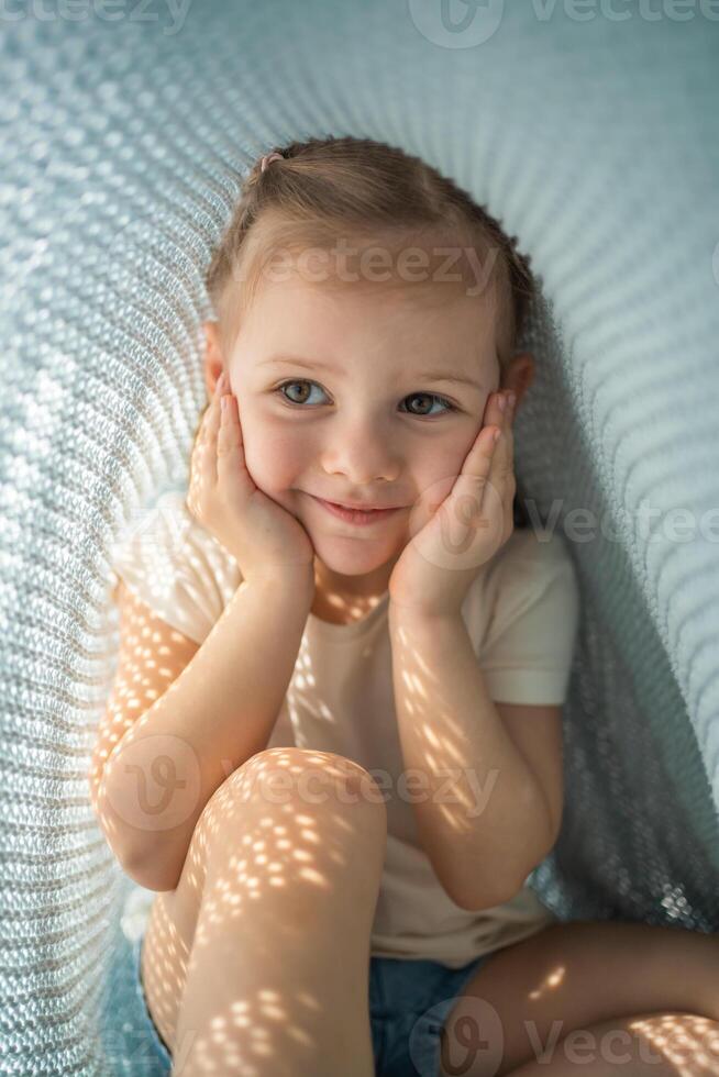 Little girl have a fun under blue knitted plaid in sunny morning photo