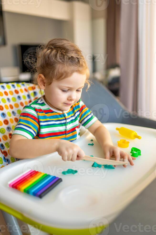 Little girl plays with multi-colored plasticine, creates different shapes photo