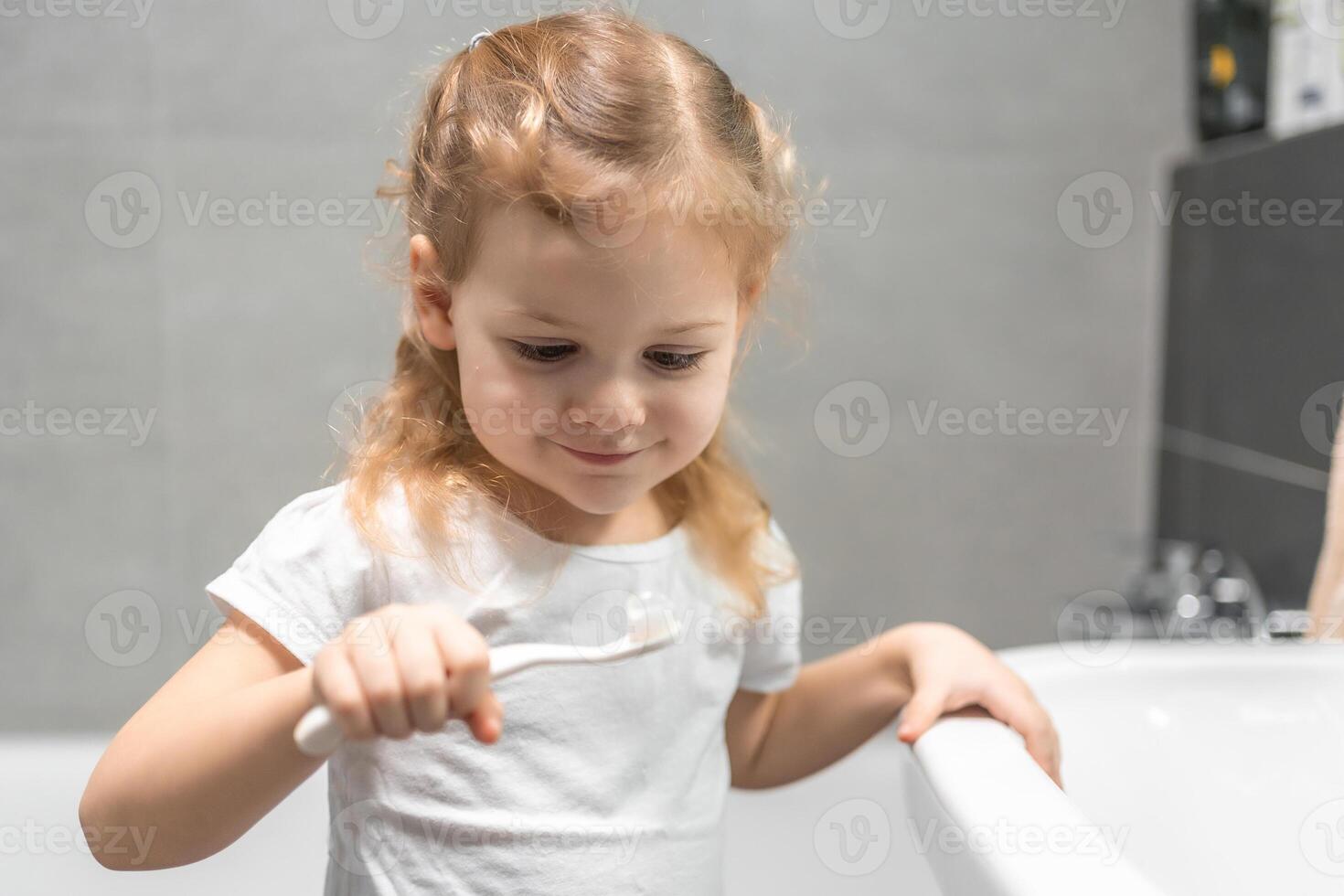 Happy toddler girl brushing teeth in the bath photo