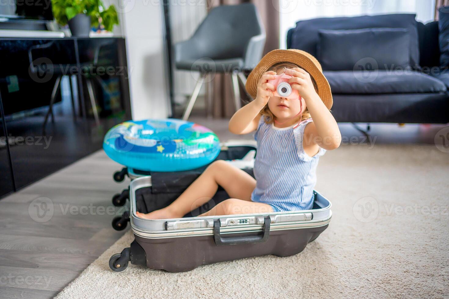 Little girl with suitcase baggage luggage and inflatable life buoy playing with toy camera and ready to go for traveling on vacation photo