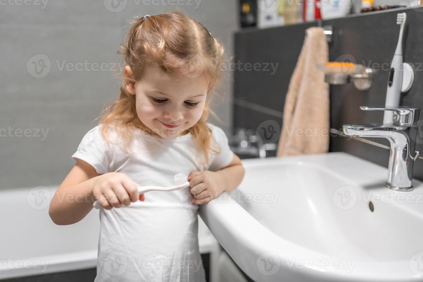 Happy toddler girl brushing teeth in the bath photo