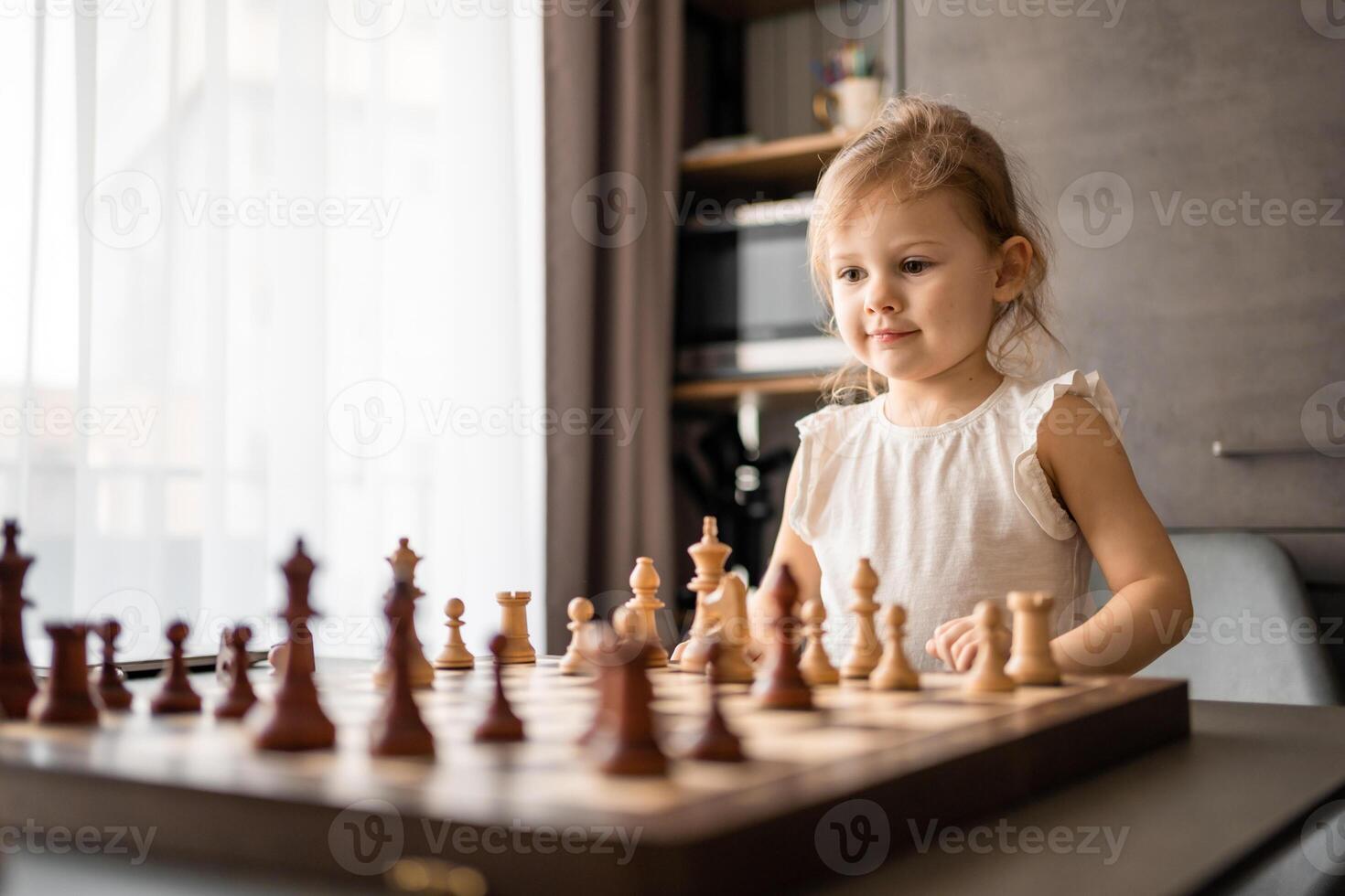 pequeño niña jugando ajedrez a el mesa en hogar cocina. el concepto temprano infancia desarrollo y educación. familia ocio, comunicación y recreación. foto