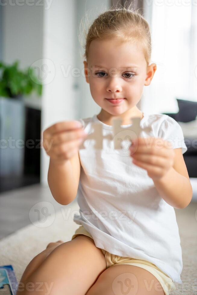 Portrait of Little blonde girl sits at home on the carpet and collects puzzles photo