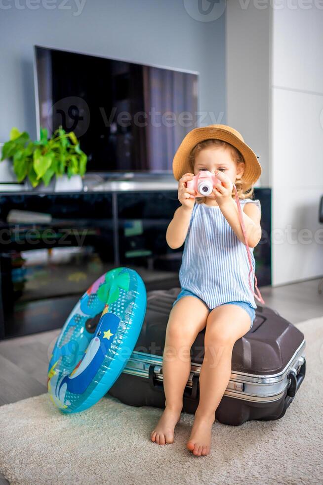 Little girl with suitcase baggage luggage and inflatable life buoy playing with toy camera and ready to go for traveling on vacation photo