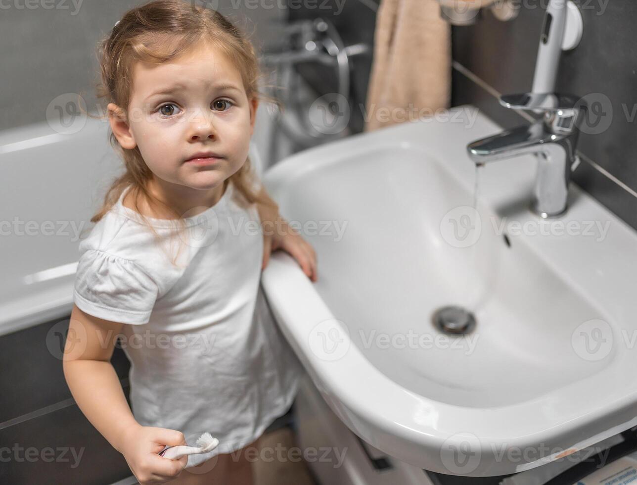 Happy toddler girl brushing teeth in the bath photo