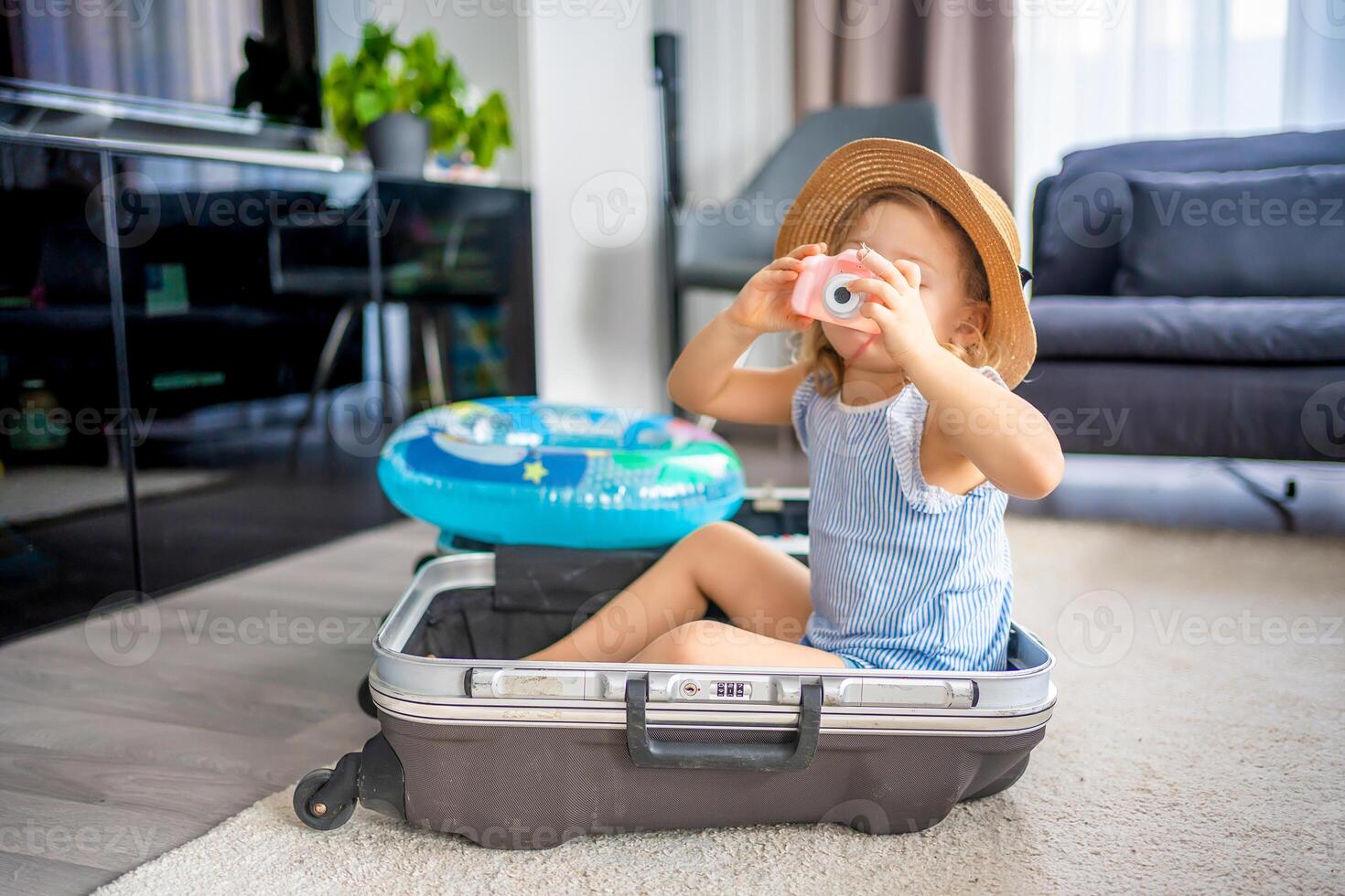 Little girl with suitcase baggage luggage and inflatable life buoy playing with toy camera and ready to go for traveling on vacation photo