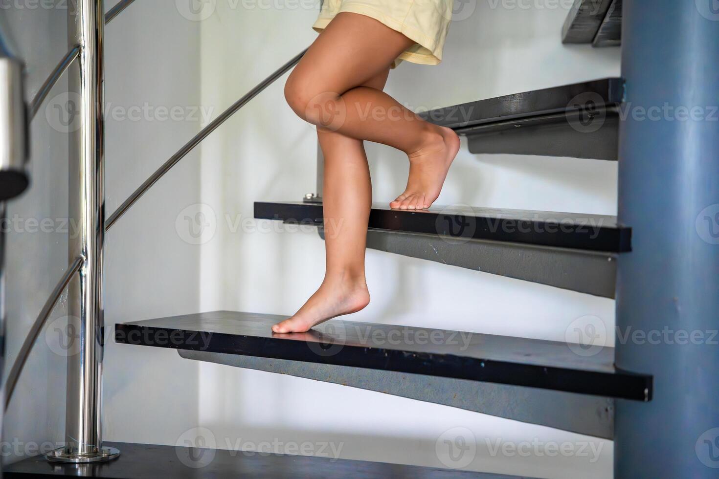 Close up view of little child girl feet going down stairs at home, child climbing spiral staircase photo