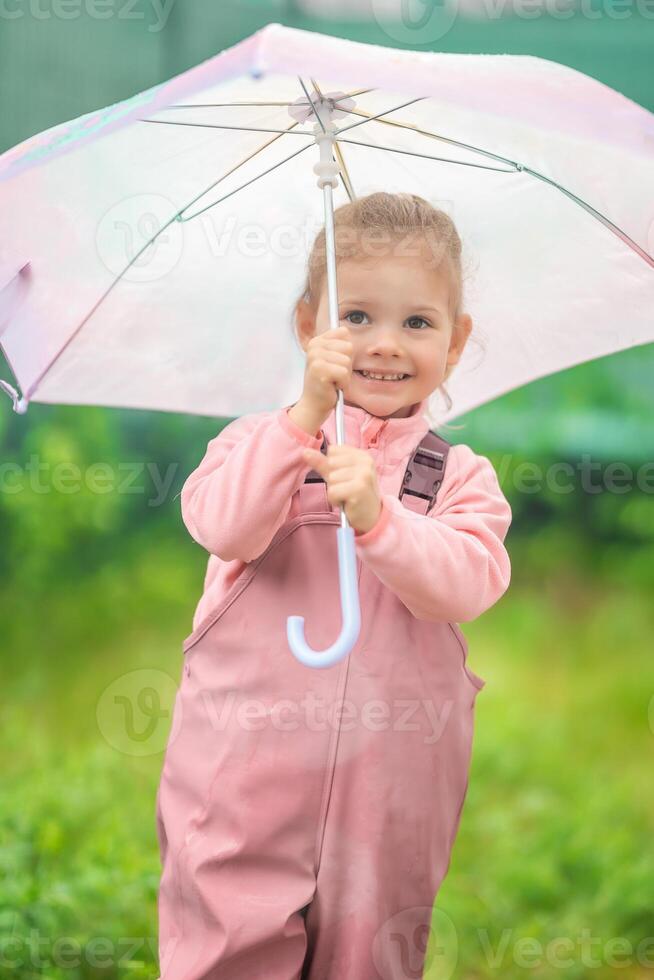 Happy laughing child girl 2-3 year old wearing waterproof clothes and holding pink umbrella have a fun on home backyard in rainy day photo