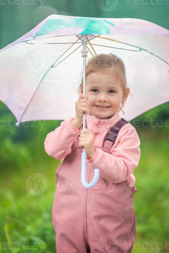 Happy laughing child girl 2-3 year old wearing waterproof clothes and holding pink umbrella have a fun on home backyard in rainy day photo