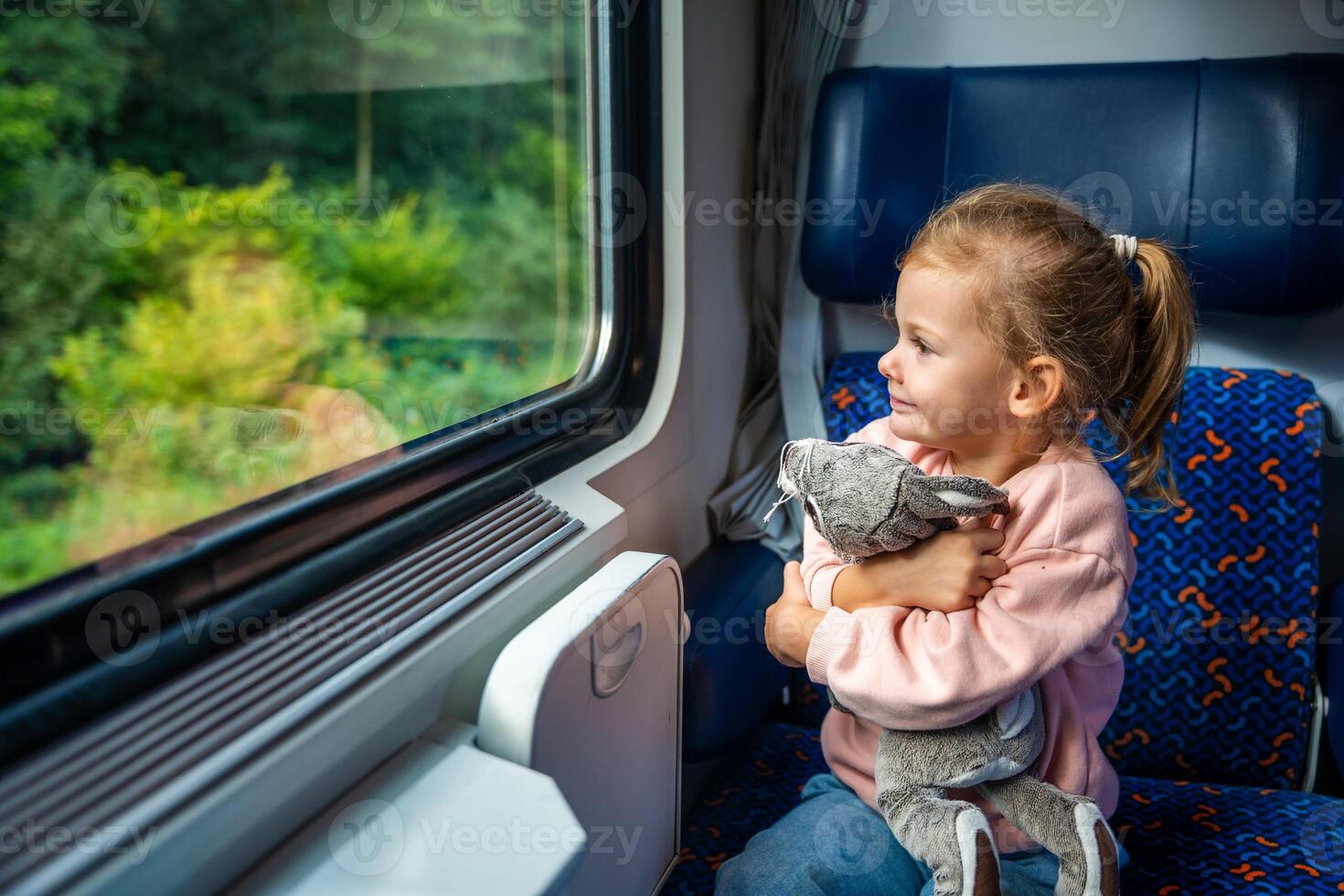 hermosa pequeño niña con juguete mirando fuera tren ventana afuera, mientras eso Moviente. de viaje por ferrocarril, Europa foto