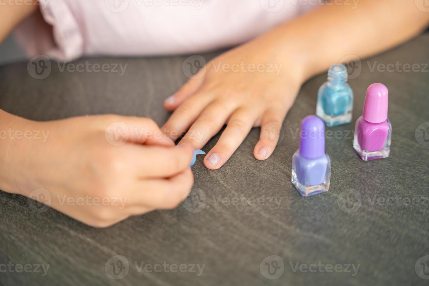 Top view of Hands of the little girl doing manicure and painting nails with colorful pink, blue and purple nail polish at home photo
