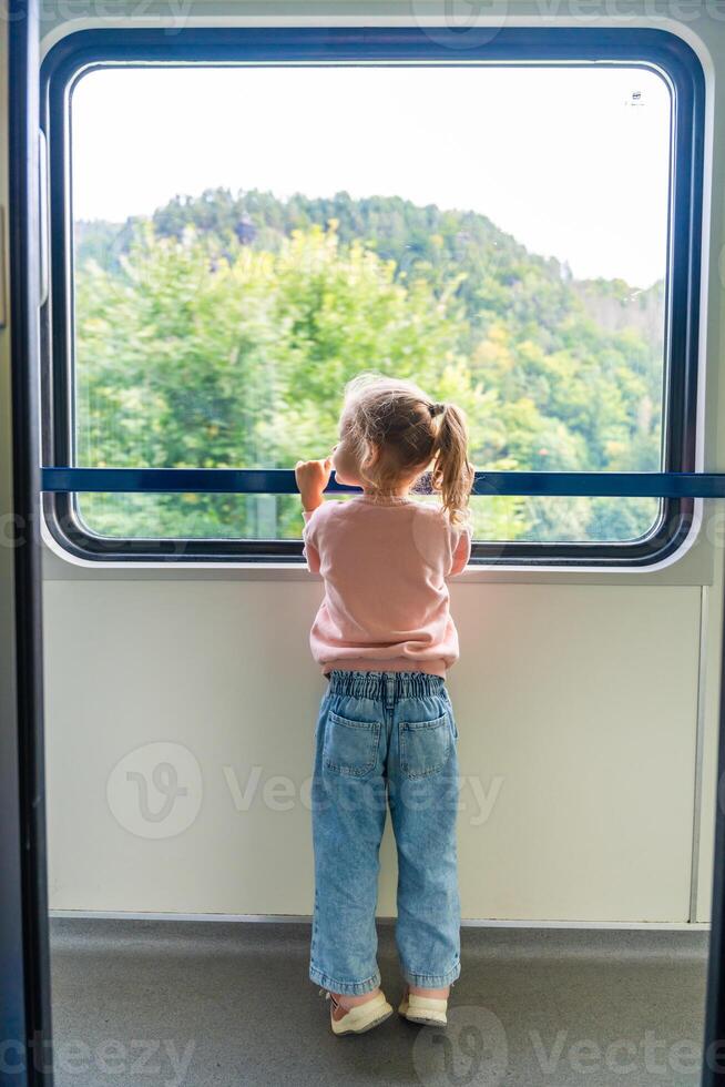 Little girl looking out train window outside, while it moving. Traveling by railway in Europe photo