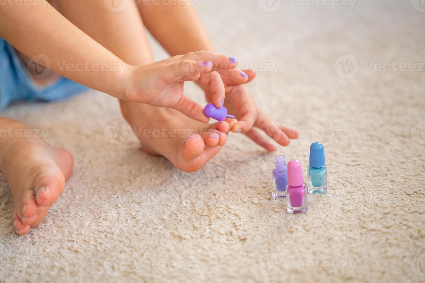 cerca arriba ver de manos de pequeño niña haciendo pedicure y pintura uñas con vistoso rosa, azul y púrpura uña polaco a hogar foto