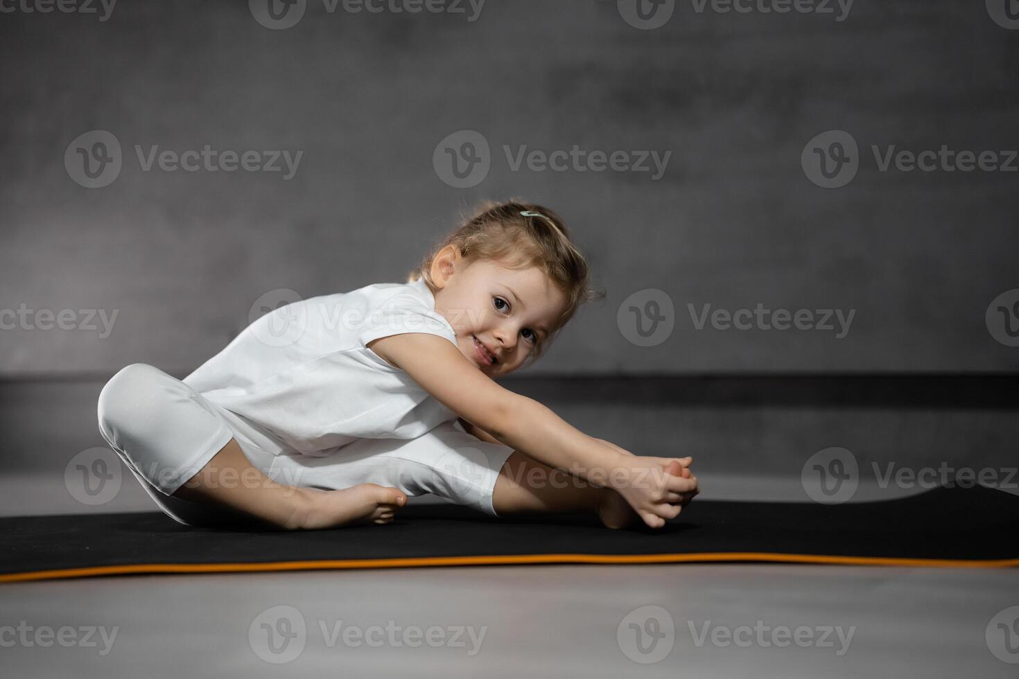 Little cute girl practicing yoga pose on grey background in dark room. High quality photo