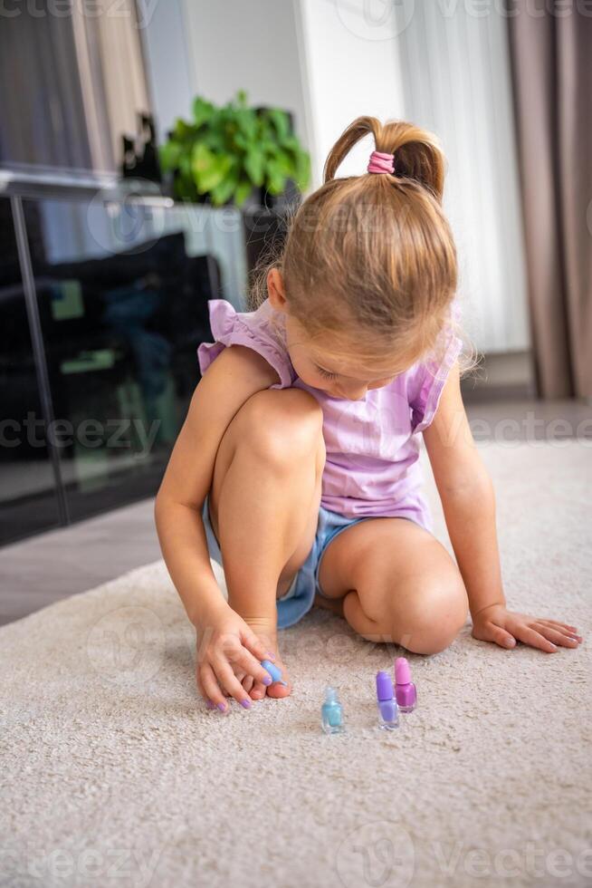 pequeño niña haciendo pedicure y pintura uñas con vistoso rosa, azul y púrpura uña polaco a hogar foto