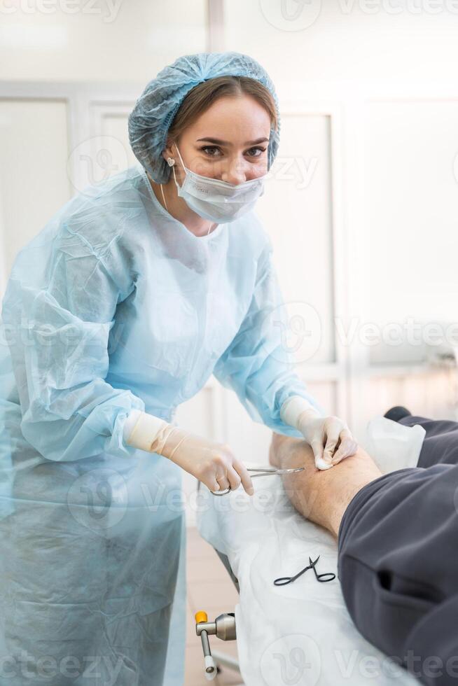 Smiling dermatologist surgeon stitching up a wound after skin surgery, close up view of operation process photo